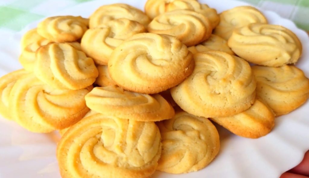 Galletas danesas de mantequilla caseras, con forma de espiral, doradas y crujientes, servidas sobre una bandeja rústica con fondo claro.